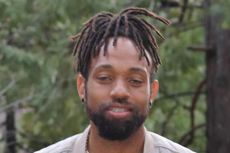 portrait image of master's degree student nick easter wearing a white top and white sport coat standing outside